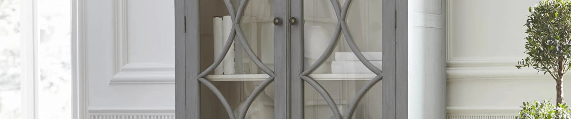 A sleek display cabinet with glass doors, showcasing decorative items in a stylish living room setting.